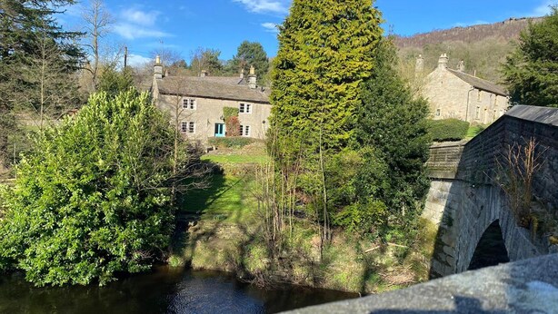 A stone bridge over a river, surrounded by lush greenery and traditional stone buildings. - Beautiful Peak District Cottage With Hot Tub (Hope Valley)