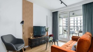 A modern living room with a sofa, a chair, a TV, and a small table with a vase. - Cozy Apartment with Balcony | Parking | Close to Park (Poznan)