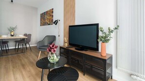 A modern living room with a flat-screen TV, a dining area with a table and chairs, a black sofa, and a potted plant. - Cozy Apartment with Balcony | Parking | Close to Park (Poznan)