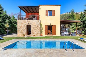 Une maison à deux étages avec une façade en pierre, un balcon et une piscine.
