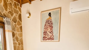 Ein Schlafzimmer mit Steinwand, einem Bett mit weißer Bettwäsche, einem Gemälde einer Frau und einem kleinen Tisch mit Kerze und Lavendel.