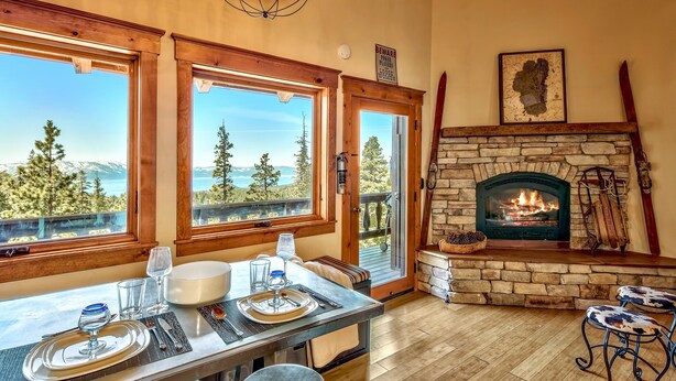 A dining area with a table set for four, large windows with a mountain view, a stone fireplace with a fire, and a ski lift in the background. - Mv8  lakeview across from Heavenly (Stateline)