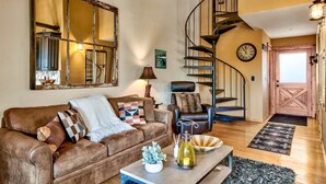 A cozy living room with a brown leather sofa, a coffee table with decorative items, a large mirror, a black leather armchair, and a spiral staircase leading to another level. - Mv8  lakeview across from Heavenly (Stateline)
