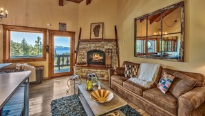 A cozy living room with a stone fireplace, wooden beams, a large mirror, and a view of the outdoors. - Mv8  lakeview across from Heavenly (Stateline)
