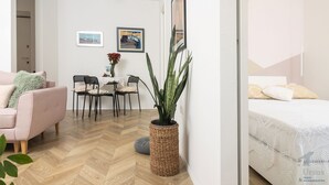 A modern, well-lit room with a wooden herringbone floor, a pink sofa, a dining table with chairs, and a large potted plant. - Mina Apartment (Split)