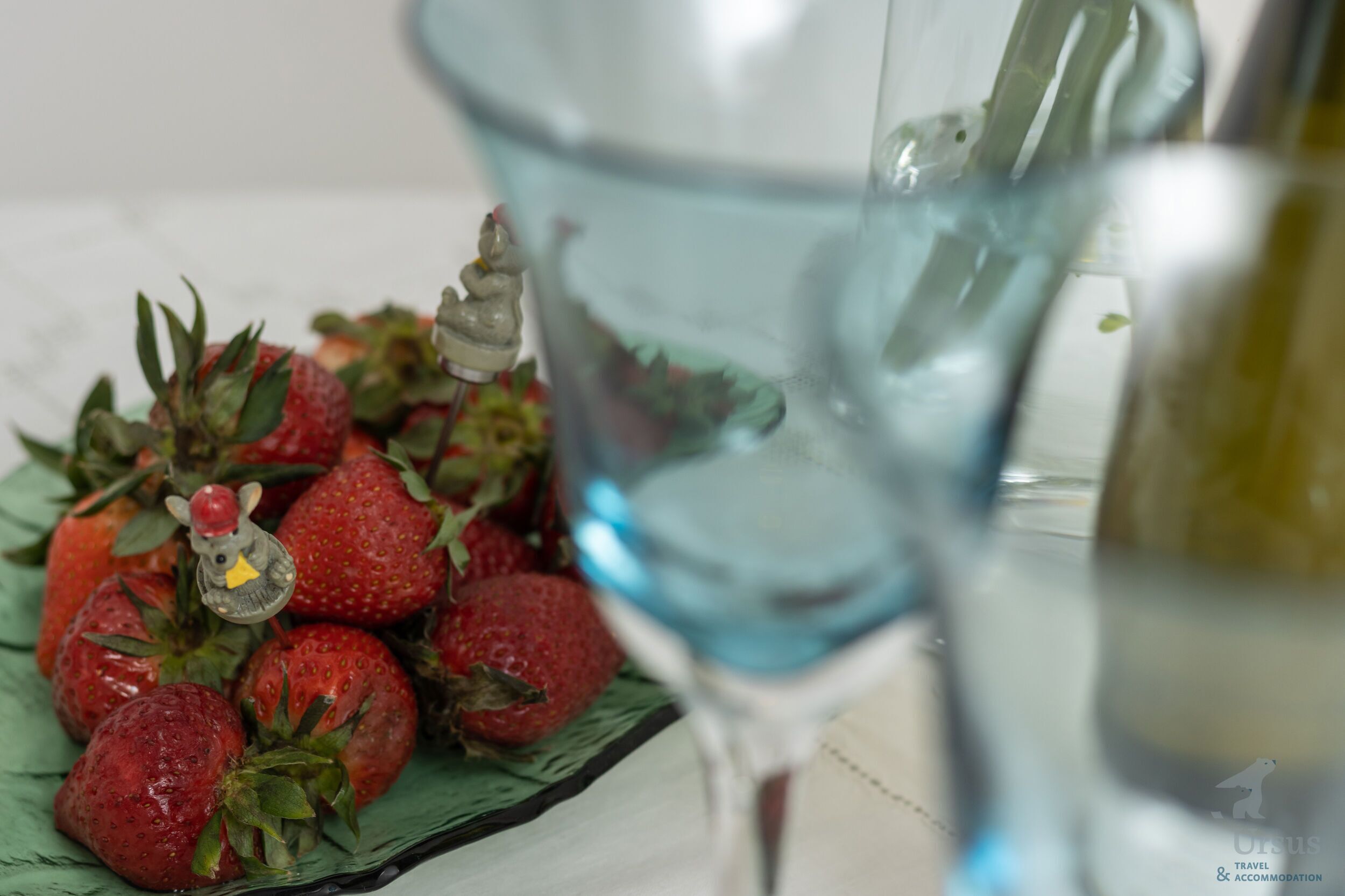 A plate of strawberries with a decorative figurine, a glass of water, and a bottle of olive oil.