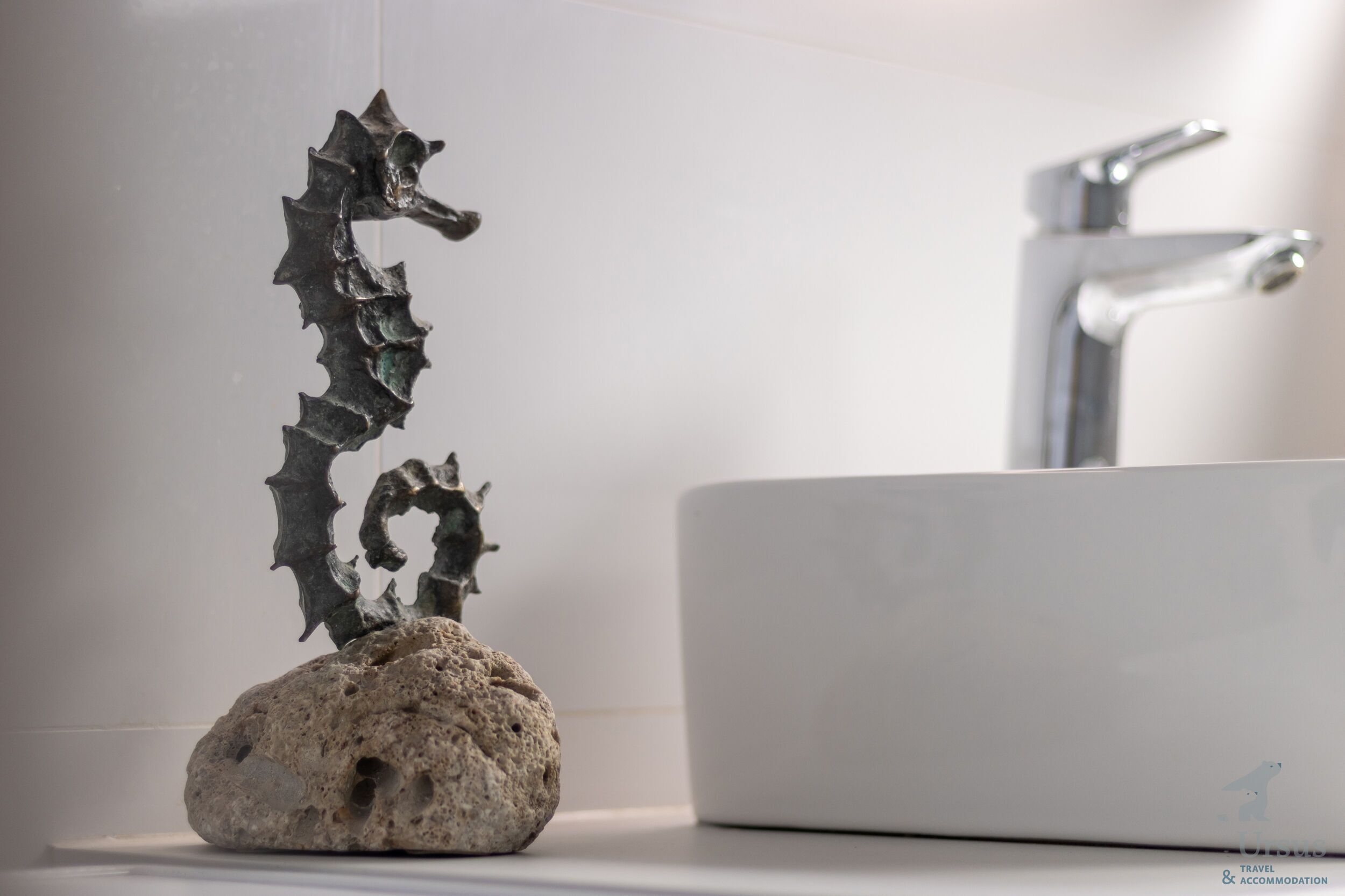 Un baño con un lavabo blanco, una escultura decorativa de caballito de mar sobre una roca y un grifo moderno.