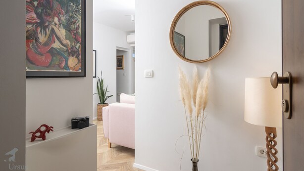 A modern interior with a framed painting, a round mirror, pampas grass in a vase, and a lamp on a wall. - Mina Apartment (Split)