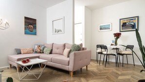 A modern living room with a pink sofa, a white coffee table, and a dining area with a table and chairs. - Mina Apartment (Split)