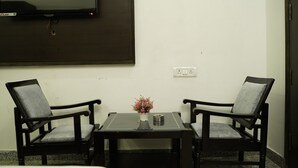 A room with two chairs, a small table with a vase of flowers, and a flat-screen TV mounted on the wall. - Hotel Anand Empire (New Delhi)