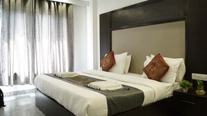 A modern hotel room with a large bed, dark headboard, and a nightstand with a lamp. - Hotel Anand Empire (New Delhi)