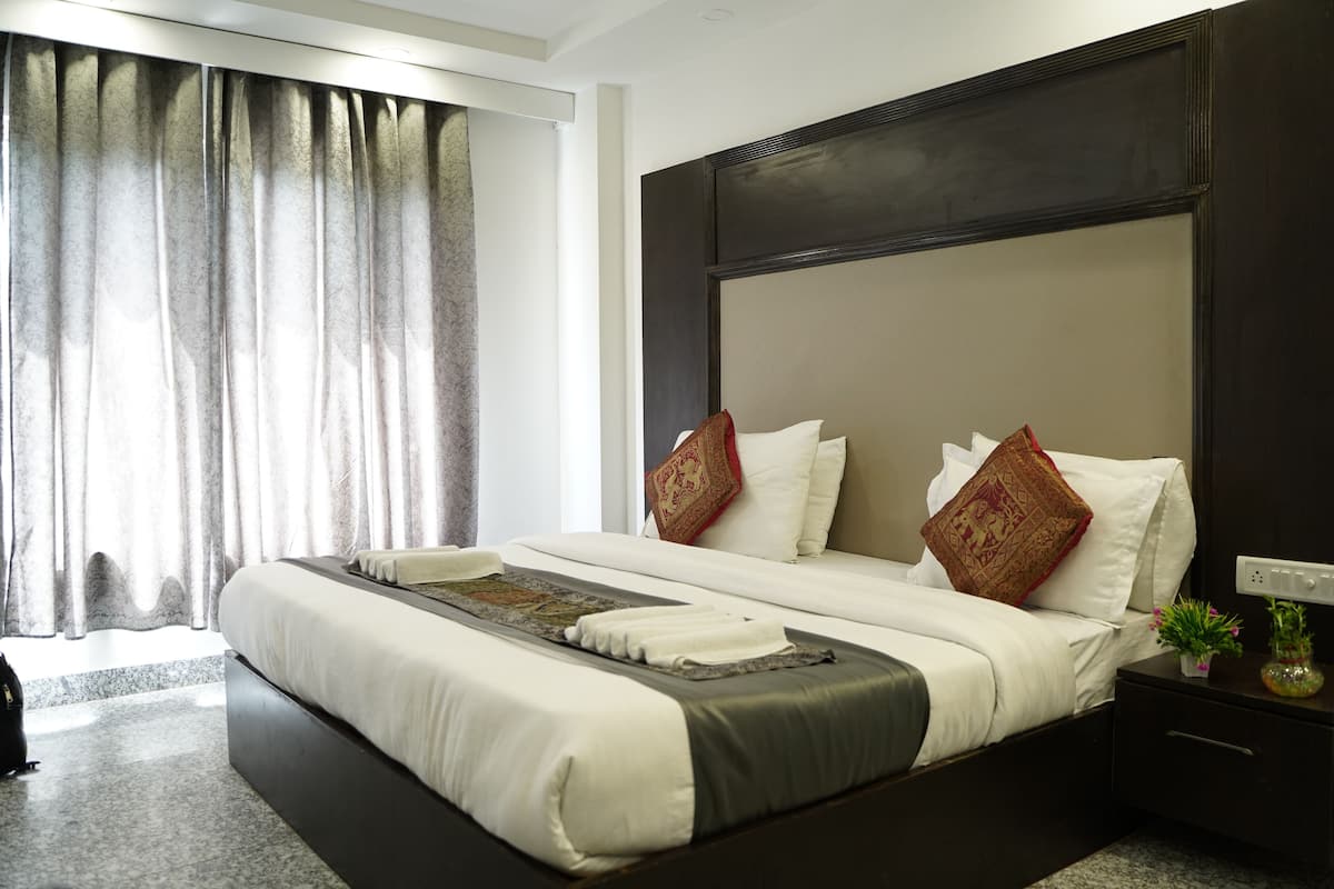 Una habitación de hotel moderna con una cama grande, cabecera oscura y una mesita de noche con lámpara.