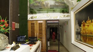 A reception area with a sign reading "Anand Enterprise," a reception desk, a computer, a plant, and a red carpet leading to a hallway. - Hotel Anand Empire (New Delhi)