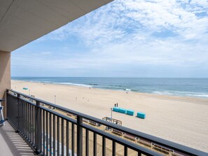 Blick auf einen Sandstrand und das Meer vom Balkon mit Geländer.