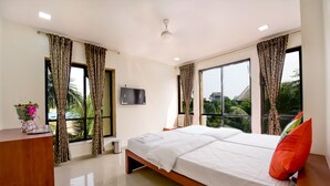 Una habitación de hotel moderna con una cama grande, un escritorio, un televisor y ventanas amplias con cortinas.