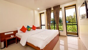 Habitación de hotel con una cama grande, una mesita de noche con teléfono y vistas a zonas verdes por las ventanas.