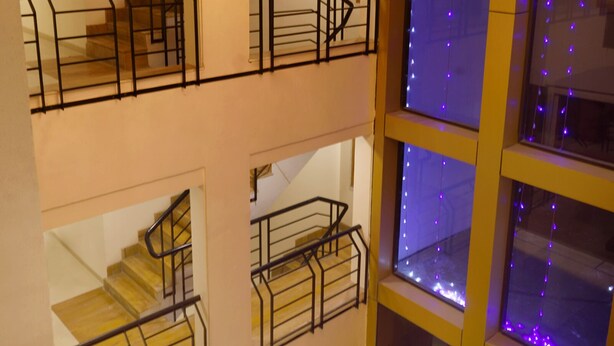 Un interior de varios niveles con candelabro, escaleras y ventanas iluminadas.