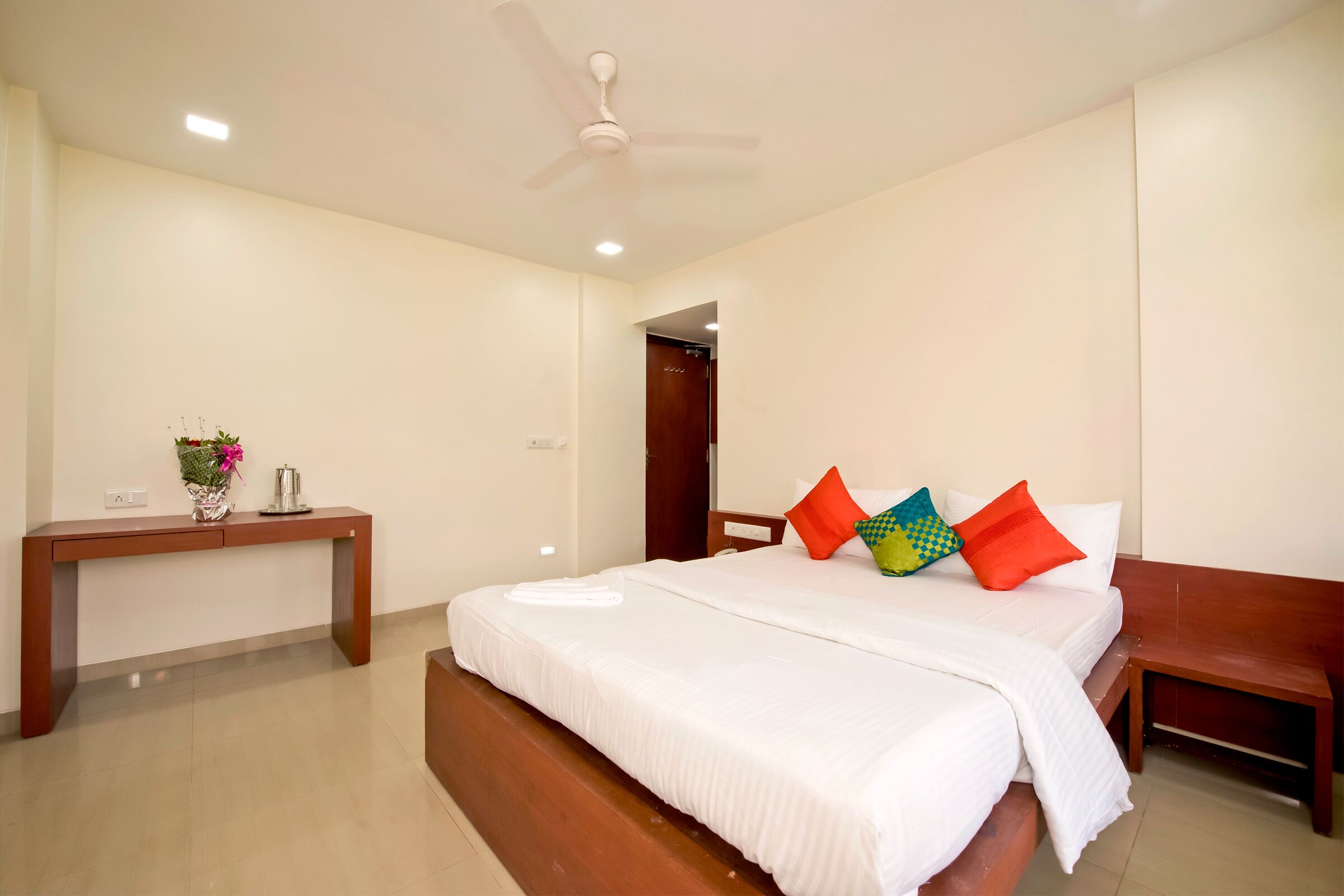 A bedroom with a large bed, a wooden nightstand, a desk, and a ceiling fan.