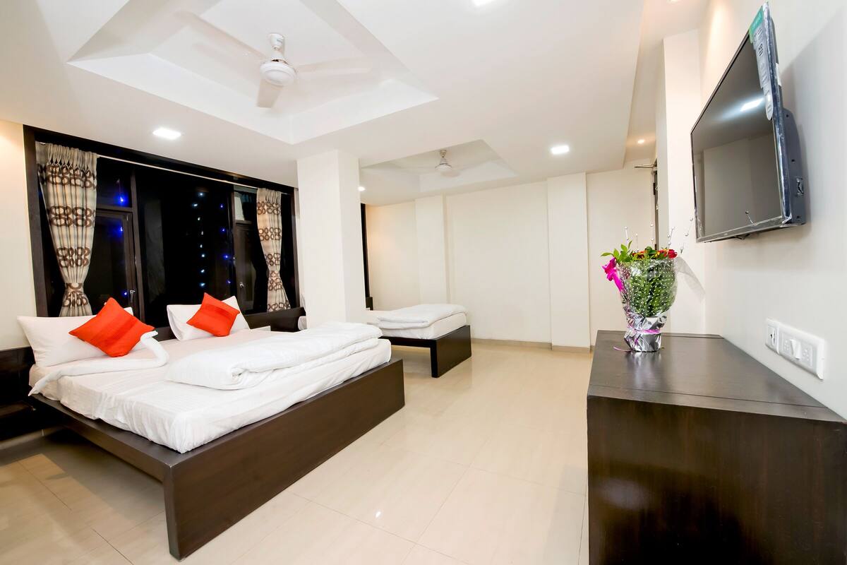Quarto moderno com uma cama grande, uma cama menor, uma televisão e um vaso decorativo.