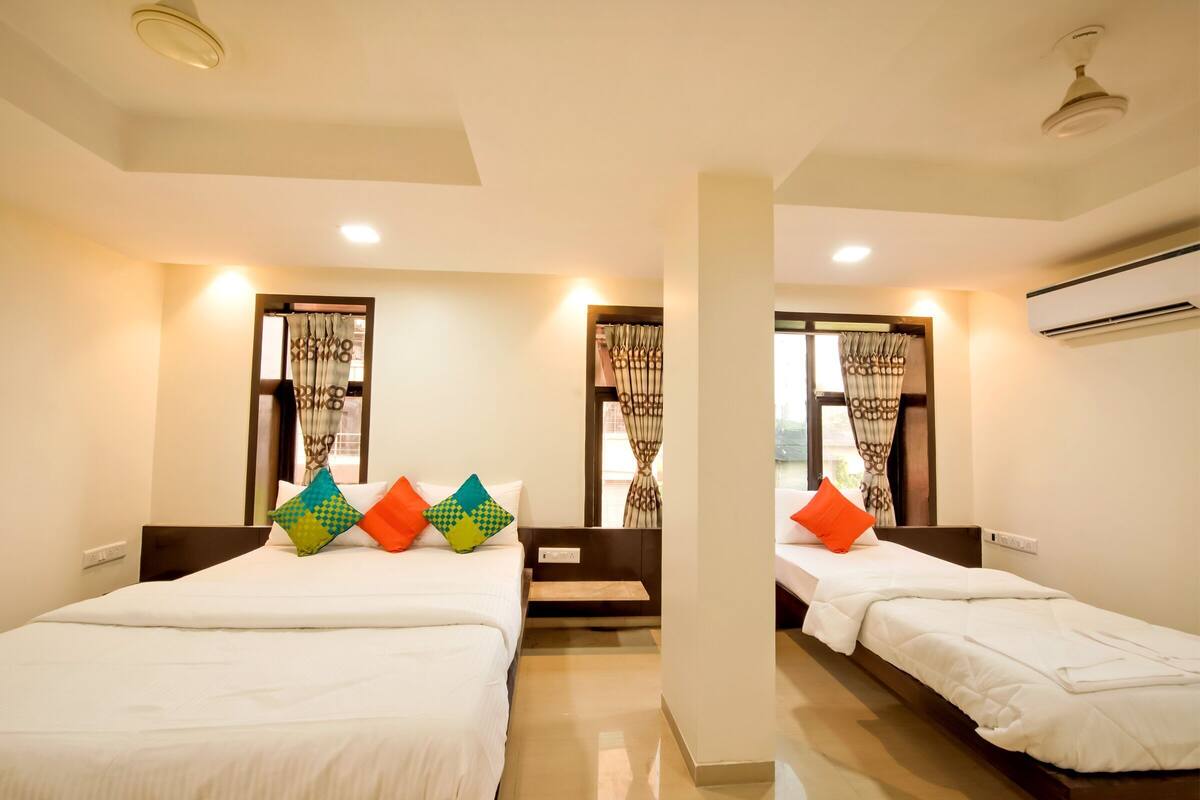 Quarto de hotel com duas camas, uma janela com cortinas, ar condicionado e um ventilador de teto.
