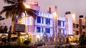 Un hotel con un letrero que dice "TRIVENI ARCH" y "HOTEL SHIVPRABHA", iluminado con luces de adorno.