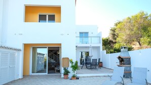 Ein modernes, zweistöckiges Gebäude mit einer Terrassenanlage, die Sitzgelegenheiten und einen Grillplatz bietet.