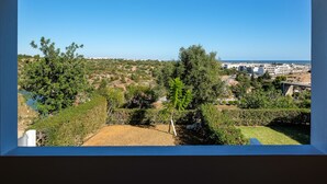 Blick aus einem Fenster auf eine Hügellandschaft mit Grünflächen und Gebäuden in der Ferne.