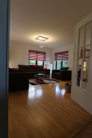 A modern living room with a sofa, armchairs, and a coffee table. There are two windows with blinds, a ceiling light, and a fireplace. - Wonderful vacation apartment on the Wieker Bodden (Wiek)