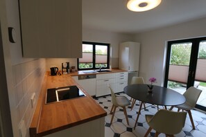 A modern kitchen with a wooden countertop, white cabinets, a built-in oven, and a dining area with a round table and chairs. - Wonderful vacation apartment on the Wieker Bodden (Wiek)
