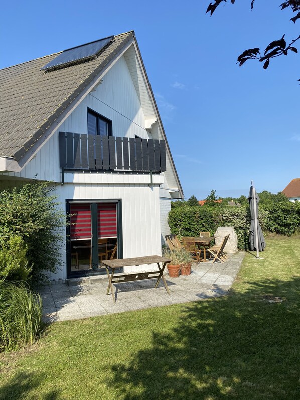 A two-story house with a balcony, a patio with outdoor furniture, and a well-maintained lawn.