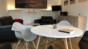 A modern living room with a round white table, two white chairs, a black sofa, and a TV on the wall. - Beautiful vacation home on Rügen (Wiek)