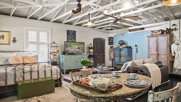 Une pièce comprenant un lit, une table ancienne avec un service à thé, une armoire bleue et un ventilateur de plafond.