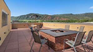 A rooftop patio with a brick fire pit, outdoor seating, and a view of green hills.