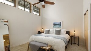 A bedroom with a bed, a ceiling fan, a window, a bedside table, and a nightstand.