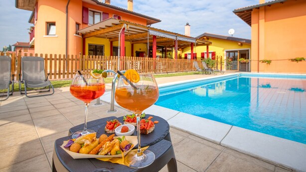 A poolside setting with a table set for two, featuring a drink and a plate of food. - HOTEL   VILLA CAMPO ROSSO (Lazise)