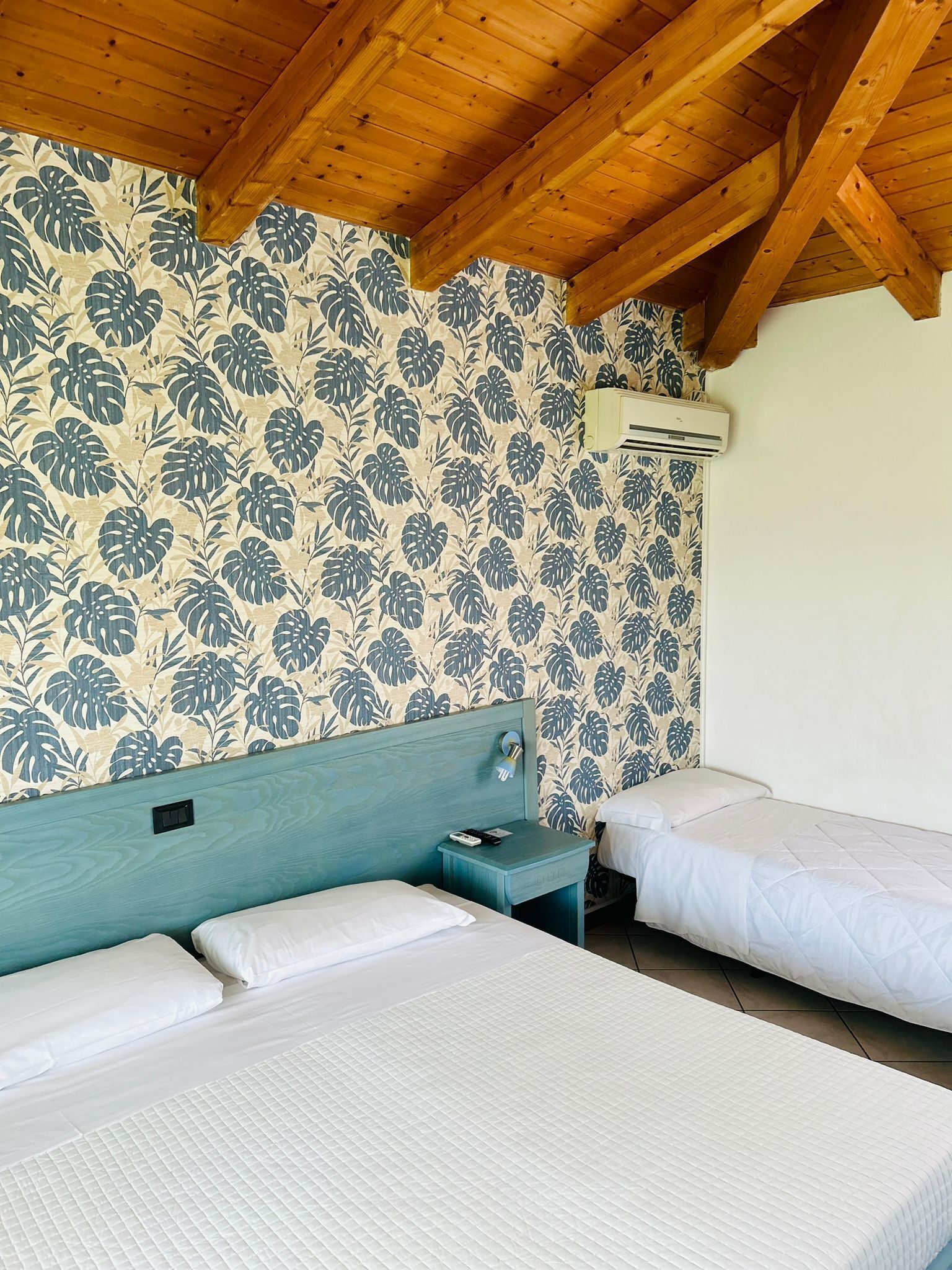 Una habitación con dos camas, vigas de madera en el techo y papel tapiz floral.