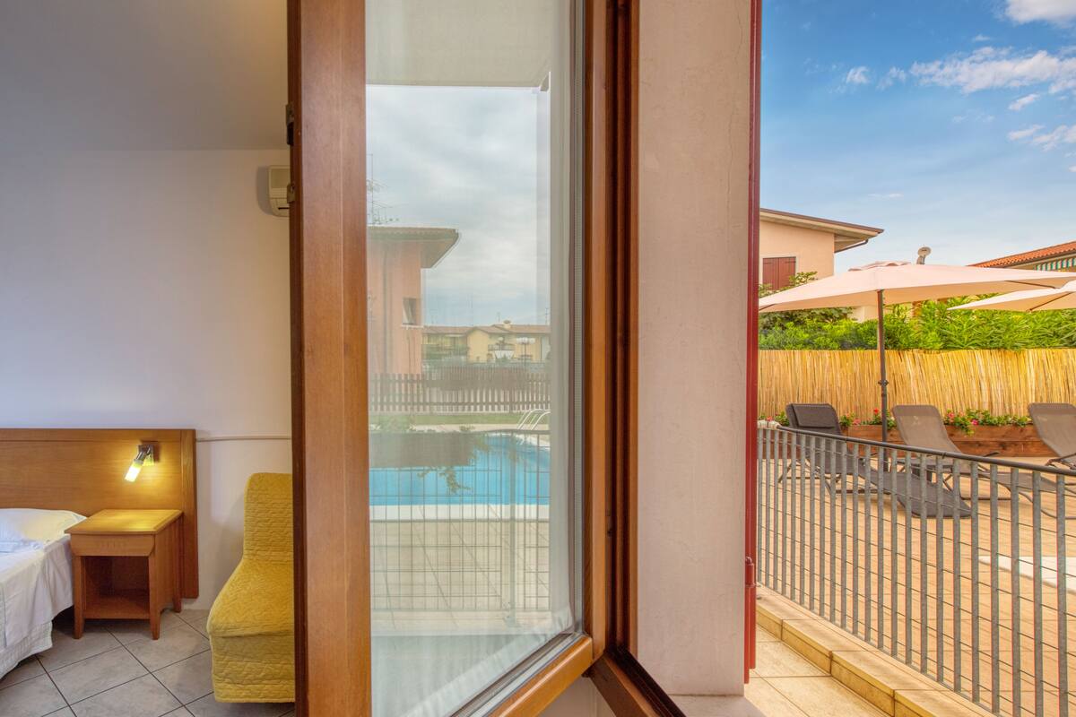 A balcony with a view of a swimming pool, a wooden chair, a small table, and a bed.