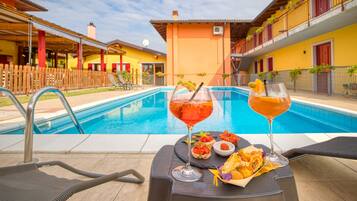 A poolside setting with two lounge chairs, a table with drinks and snacks, and a pool in the background.