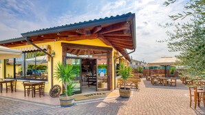 An outdoor seating area with wooden tables and chairs, potted plants, and a covered patio. - HOTEL   VILLA CAMPO ROSSO (Lazise)