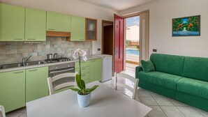 A kitchen with green cabinets, a white table with a potted orchid, and a green sofa in a living area. - HOTEL   VILLA CAMPO ROSSO (Lazise)
