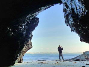 A person standing in a natural rock formation with a view of the sea.