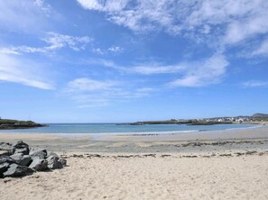 A beach with a clear sky, rocky foreground, and distant buildings. - Lligwy House - Charming 3-bed House in Holyhead (Holyhead)