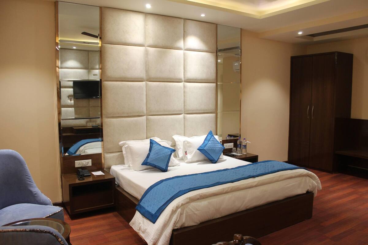 A hotel room with a large bed, a mirror, a wardrobe, and a television.