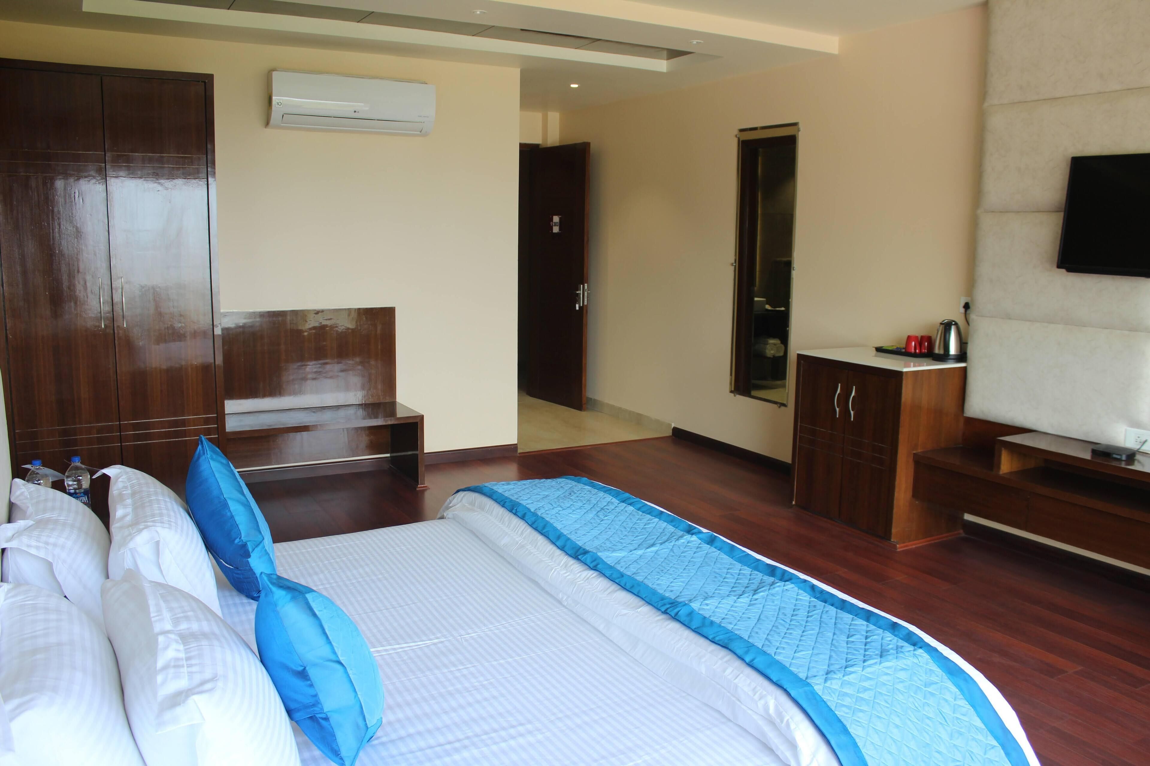 Habitación de hotel con una cama grande, un armario de madera, un escritorio pequeño con un televisor y una puerta que da a otra habitación.