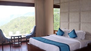 A hotel room with a large bed, two chairs, a small table, and a view of a forested mountain. - Mastiff Hotel Dalhousie (Dalhousie)