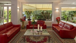 A room with two red leather sofas, a glass coffee table, and a large window with a view of greenery. - Hotel Scandinavia (Massa)
