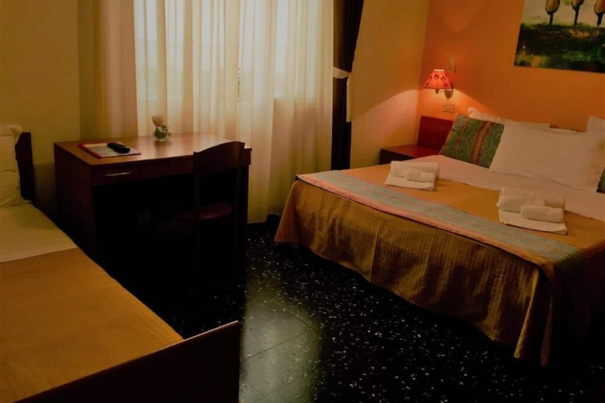 Una habitación de hotel con cama, escritorio, silla, mesita de noche y lámpara.