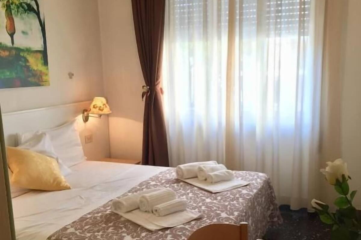 Habitación de hotel con cama, escritorio, silla, lámpara y un cuadro en la pared.