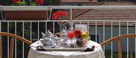 A table set with tea, coffee, and fruit on a balcony with a tiled roof and flowers in the background.