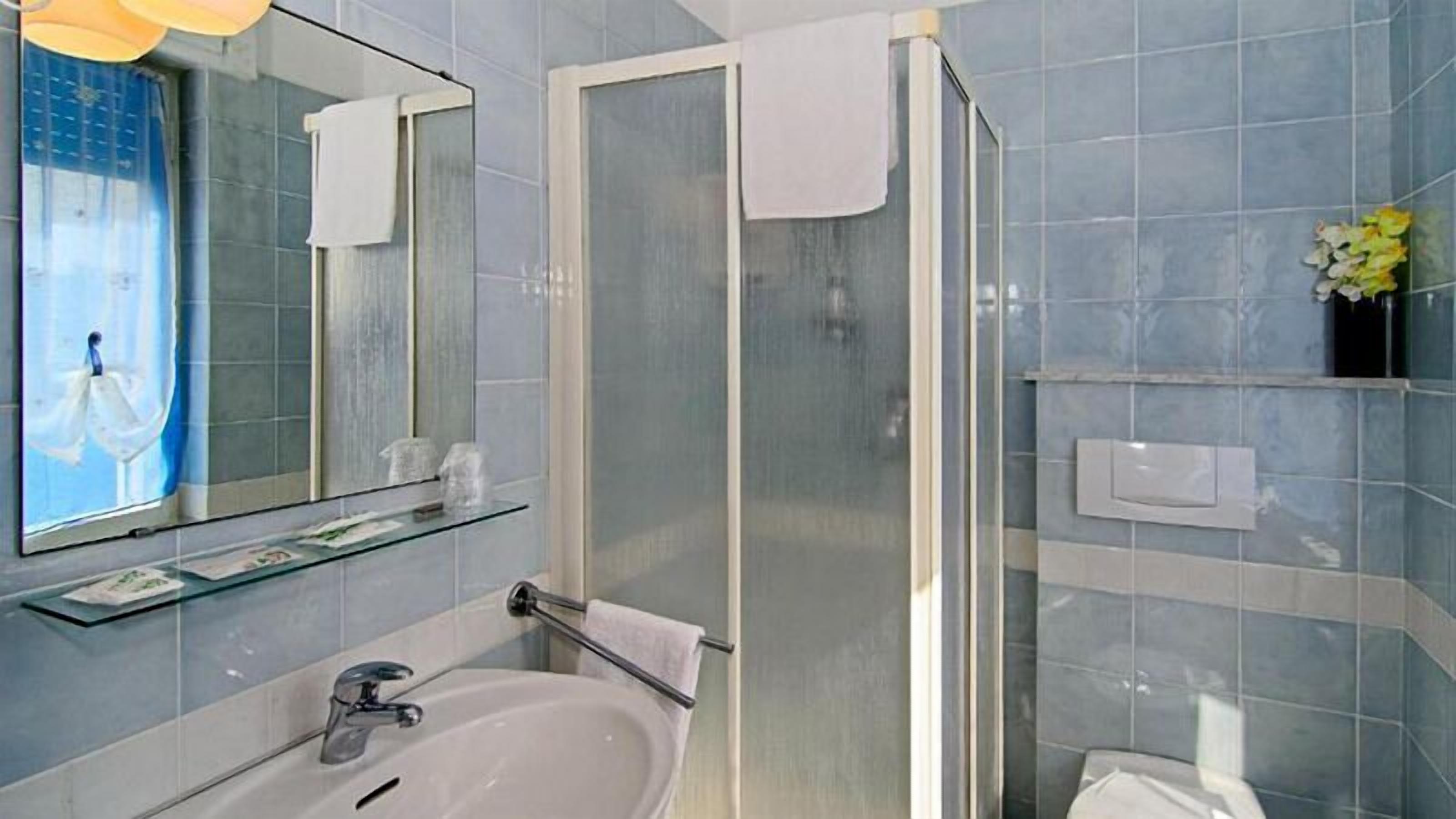 Uma casa de banho com cabine de chuveiro em vidro, banheira, pia com espelho e um armário com artigos de higiene pessoal.